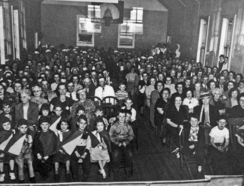 The audience for an elementary stage production in 1950. Note the basketball hoop.
